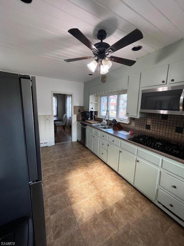 kitchen with dark countertops, backsplash, white cabinetry, a sink, and black appliances