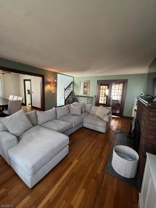 living area with stairs, a textured ceiling, a brick fireplace, and wood finished floors