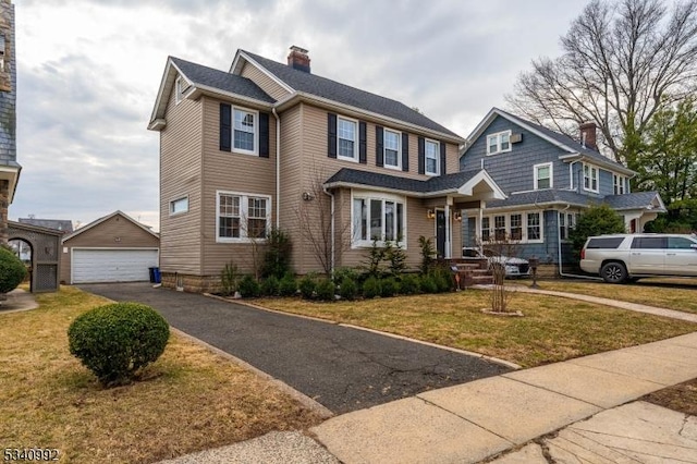 view of front of house featuring a garage, a front yard, a chimney, and an outbuilding