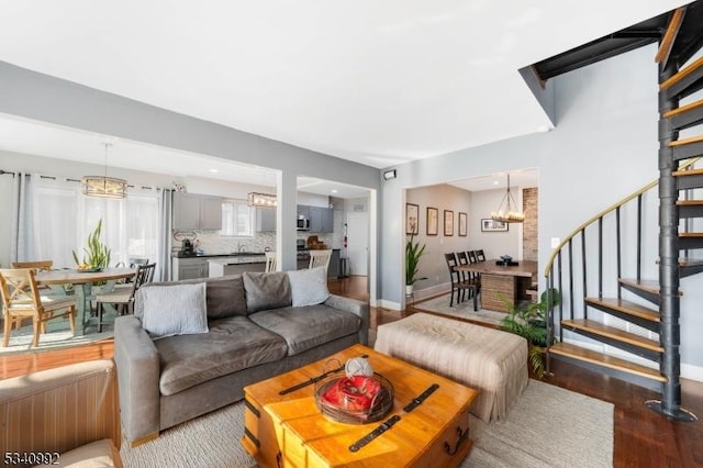 living room featuring stairs, baseboards, wood finished floors, and an inviting chandelier