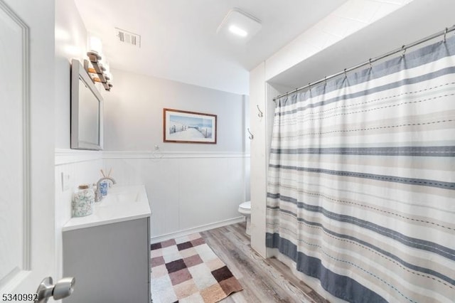 bathroom featuring visible vents, wainscoting, toilet, wood finished floors, and vanity