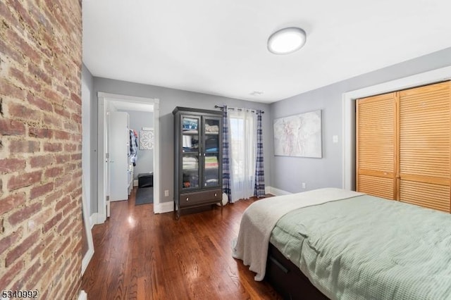 bedroom with a closet, brick wall, baseboards, and wood finished floors