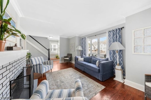 living area with crown molding, a brick fireplace, wood finished floors, baseboards, and stairs