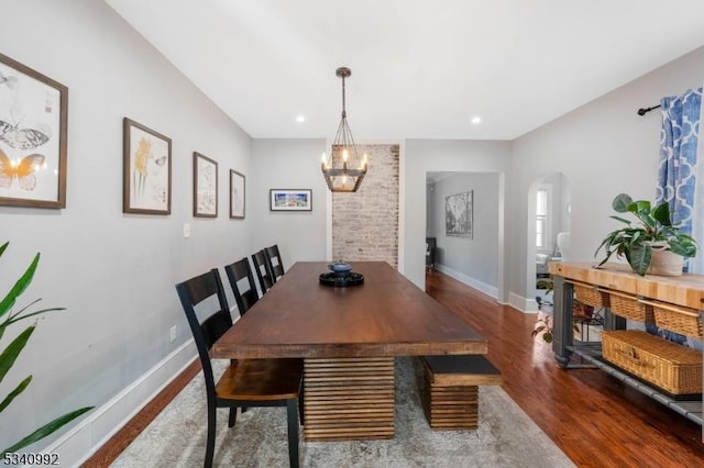 dining area featuring baseboards, arched walkways, a chandelier, and wood finished floors