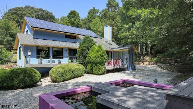 back of property with a shingled roof, a chimney, a wooden deck, and solar panels