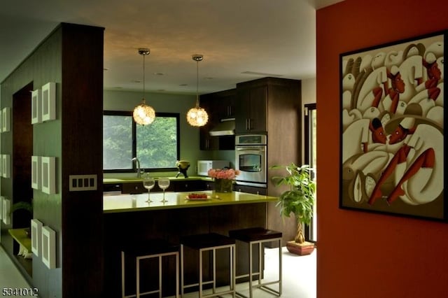 kitchen with range hood, pendant lighting, light countertops, stainless steel oven, and a kitchen breakfast bar