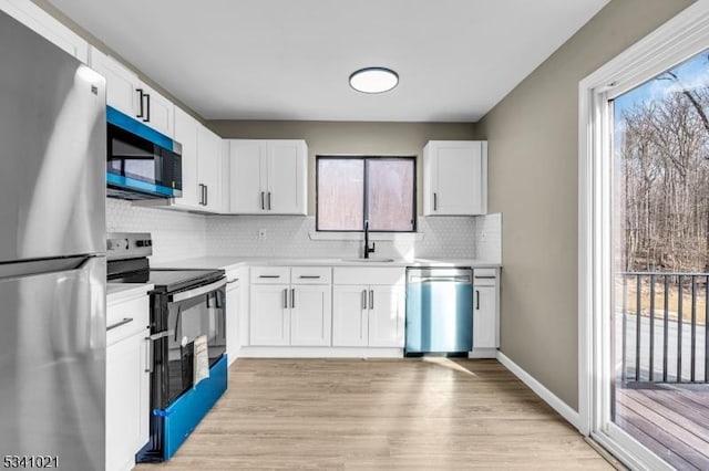 kitchen with stainless steel appliances, a sink, light countertops, light wood-type flooring, and backsplash