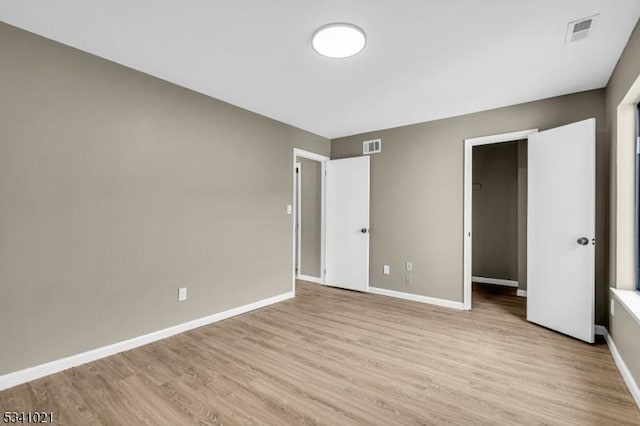 unfurnished bedroom with a walk in closet, wood finished floors, visible vents, and baseboards