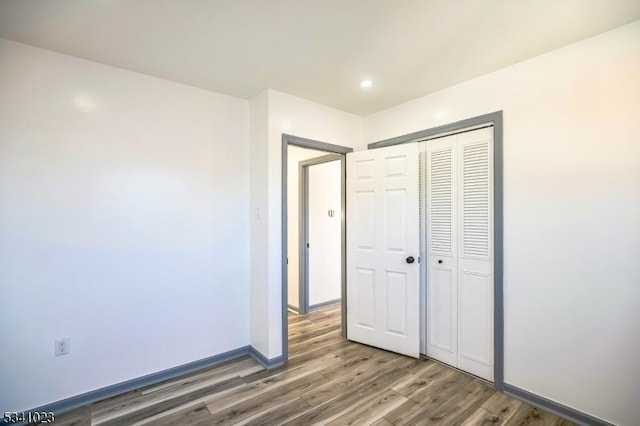 unfurnished bedroom featuring recessed lighting, a closet, baseboards, and wood finished floors