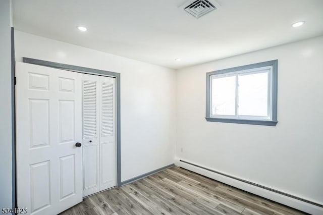 unfurnished bedroom featuring visible vents, baseboard heating, light wood-style flooring, recessed lighting, and a closet