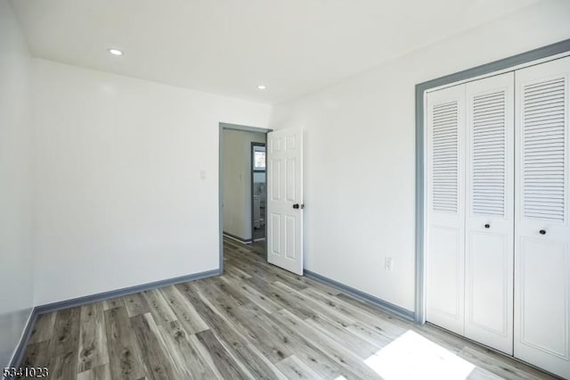 unfurnished bedroom featuring a closet, recessed lighting, light wood finished floors, and baseboards