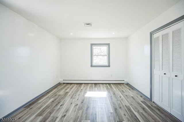 unfurnished bedroom featuring visible vents, light wood-style flooring, a baseboard heating unit, a closet, and baseboards