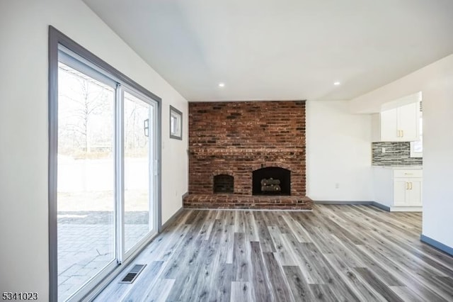 unfurnished living room with plenty of natural light, a brick fireplace, light wood-style floors, and visible vents