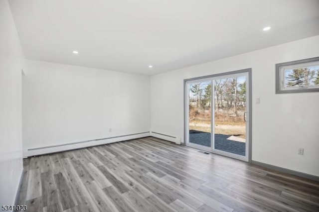 spare room with a baseboard heating unit, plenty of natural light, and wood finished floors