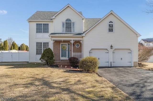 traditional-style home featuring driveway, brick siding, an attached garage, fence, and a front yard