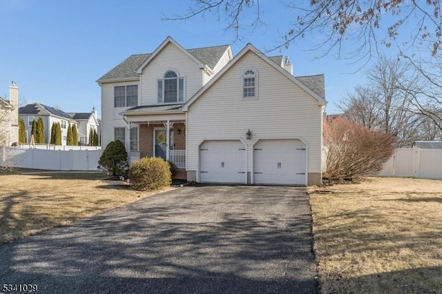 traditional home with aphalt driveway, a garage, brick siding, fence, and a front lawn