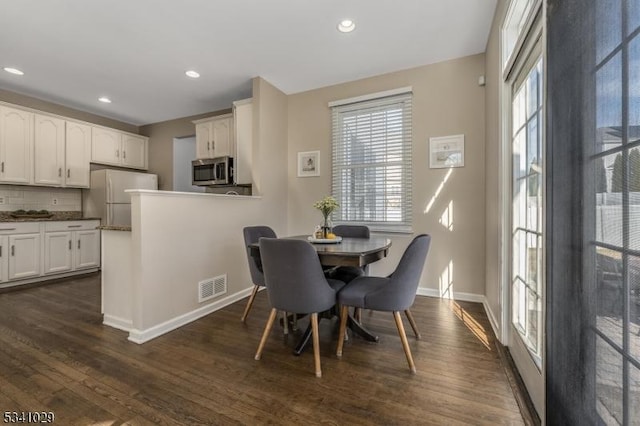 dining space featuring dark wood-type flooring, a healthy amount of sunlight, visible vents, and baseboards