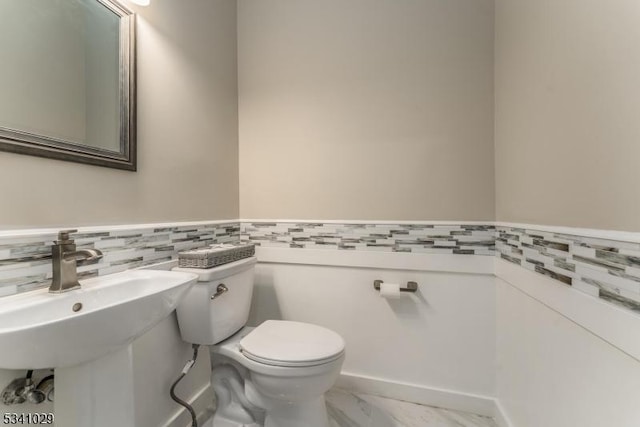 half bath with marble finish floor, wainscoting, and toilet