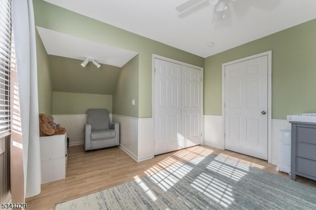 bedroom with ceiling fan, wood finished floors, vaulted ceiling, a closet, and wainscoting