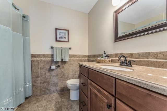 full bathroom featuring a wainscoted wall, tile walls, toilet, vanity, and a shower with curtain