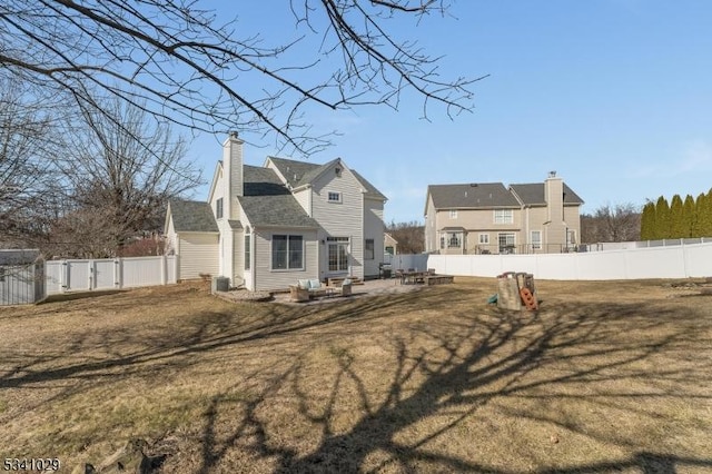 rear view of house featuring a patio area, a fenced backyard, a chimney, and a yard