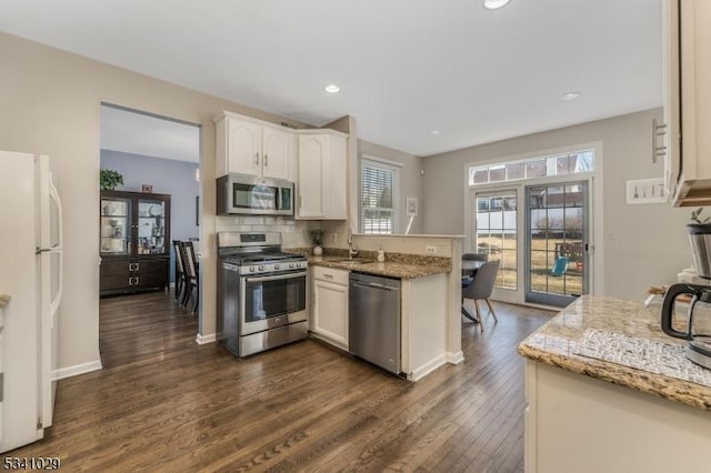 kitchen with appliances with stainless steel finishes, dark wood-style flooring, light stone countertops, white cabinetry, and a sink