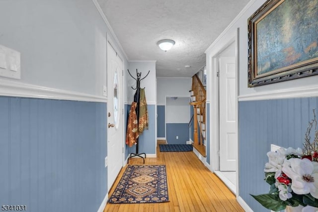 hallway with light wood-type flooring, a wainscoted wall, stairway, and a textured ceiling