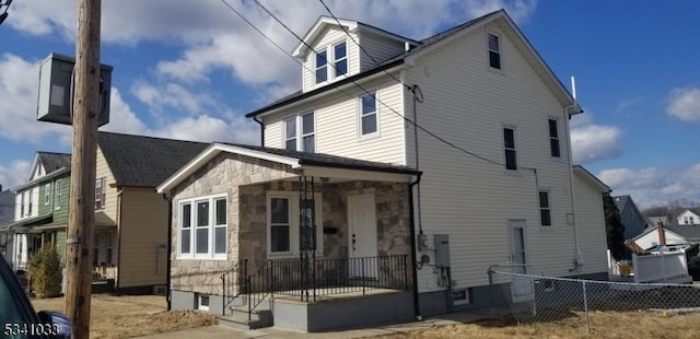 view of front of home featuring stone siding, fence, and covered porch