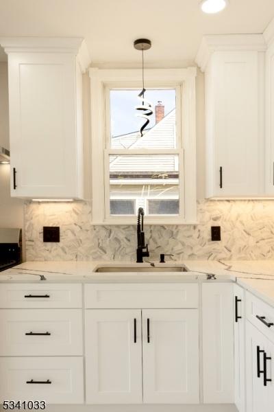 kitchen with light stone countertops, decorative backsplash, white cabinets, and a sink