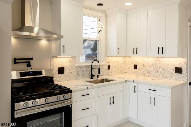 kitchen featuring gas range, light stone countertops, wall chimney range hood, white cabinetry, and a sink