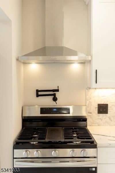 interior details featuring wall chimney exhaust hood, stainless steel range with gas cooktop, white cabinetry, and decorative backsplash