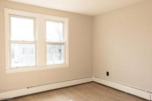 spare room featuring baseboard heating, wood finished floors, and a wealth of natural light