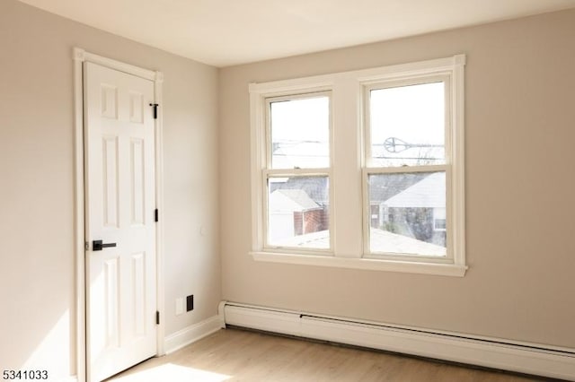 empty room with a baseboard heating unit, light wood-style floors, and baseboards