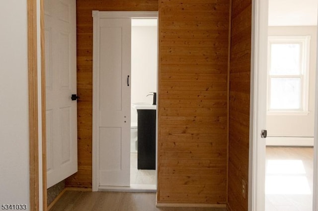 hallway featuring light wood-type flooring, wood walls, and a baseboard radiator