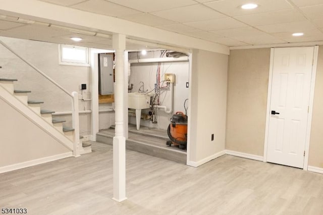 below grade area with stairs, a drop ceiling, baseboards, and wood finished floors