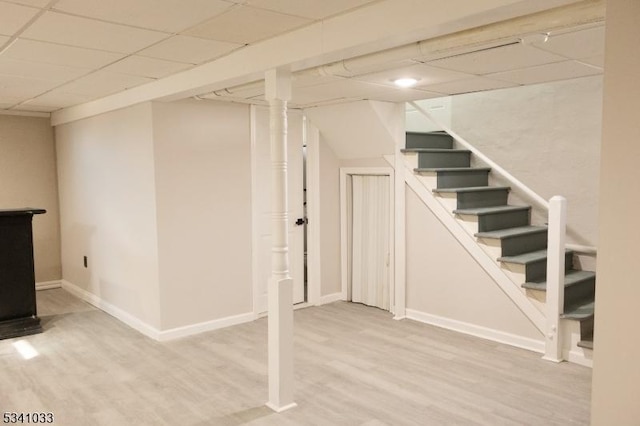 finished below grade area with light wood finished floors, stairway, a paneled ceiling, and baseboards