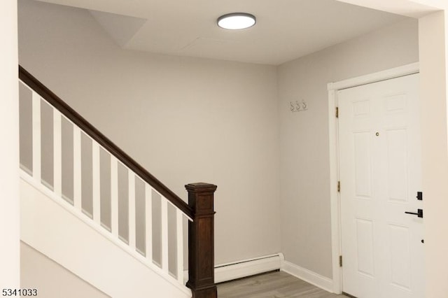 foyer entrance featuring stairway, baseboards, a baseboard heating unit, and wood finished floors