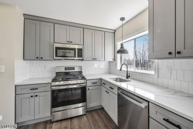 kitchen with light stone counters, gray cabinets, stainless steel appliances, and a sink