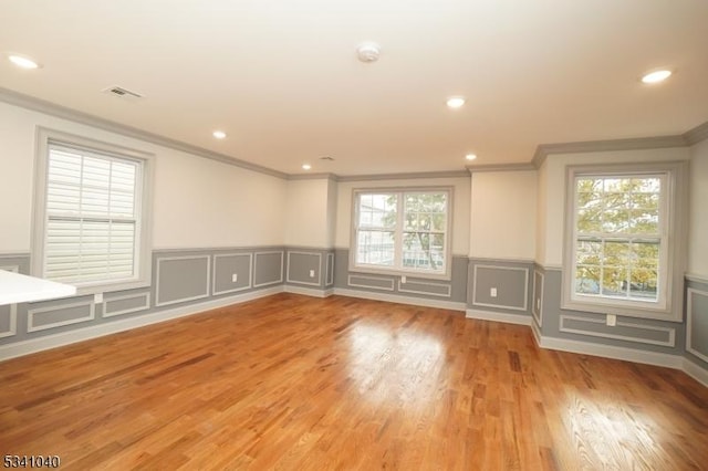 spare room with ornamental molding, a wealth of natural light, visible vents, and light wood-style flooring