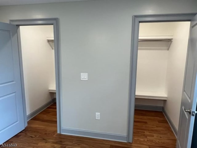 unfurnished bedroom with a walk in closet, a closet, baseboards, and wood finished floors