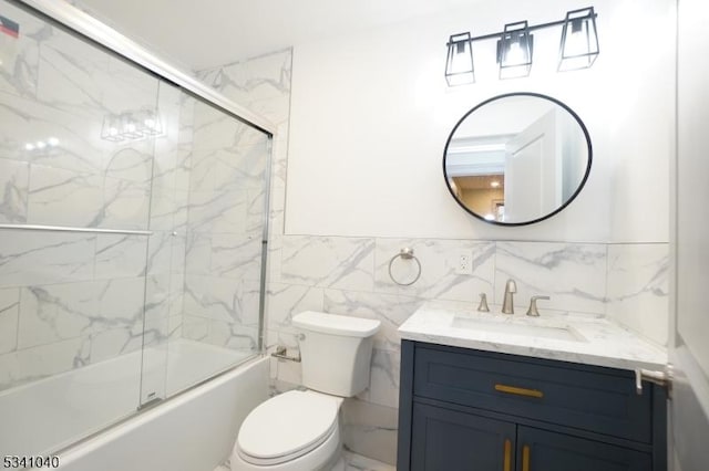 full bathroom with toilet, shower / bath combination with glass door, vanity, tile walls, and wainscoting