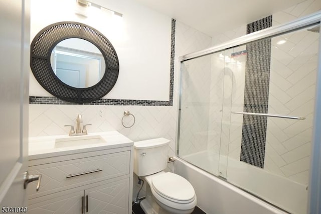 full bath featuring combined bath / shower with glass door, vanity, toilet, and tile walls