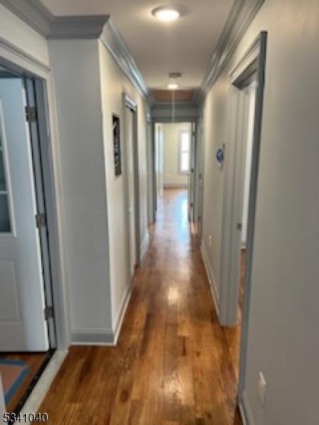 hall featuring baseboards, wood finished floors, and crown molding