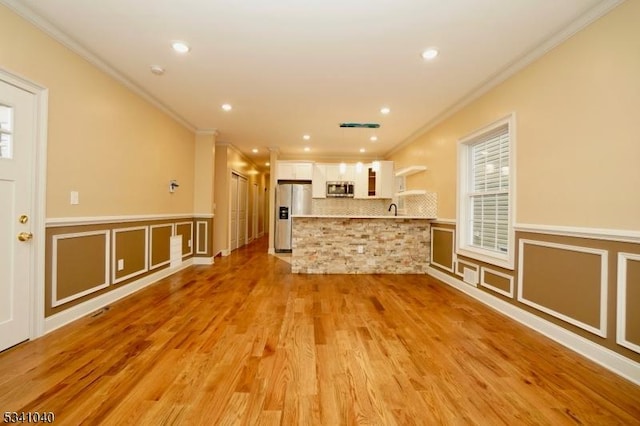 unfurnished living room featuring a wainscoted wall, light wood-style flooring, ornamental molding, and recessed lighting