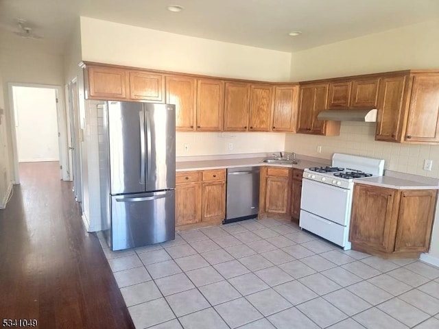 kitchen featuring under cabinet range hood, stainless steel appliances, a sink, light countertops, and brown cabinetry