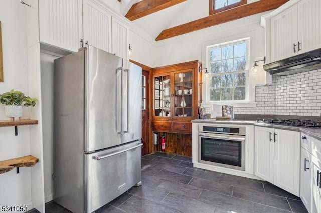 kitchen with under cabinet range hood, tasteful backsplash, white cabinetry, appliances with stainless steel finishes, and vaulted ceiling