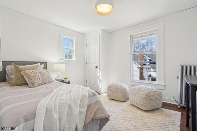 bedroom featuring multiple windows, radiator, baseboards, and dark wood-style flooring