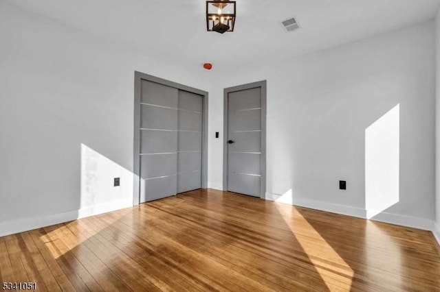 unfurnished bedroom featuring visible vents, baseboards, and wood finished floors