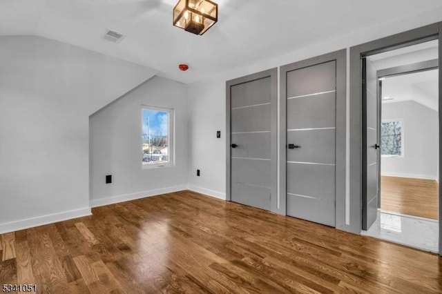 unfurnished bedroom featuring lofted ceiling, visible vents, baseboards, and wood finished floors