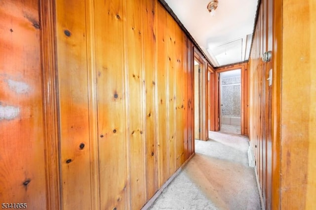 hall with wooden walls, attic access, and light colored carpet